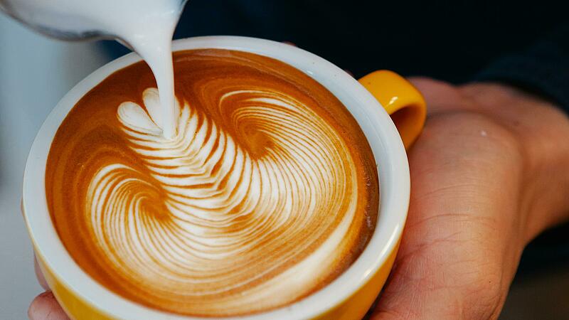 Barista der mit Milch latte art in den Kaffee gießt